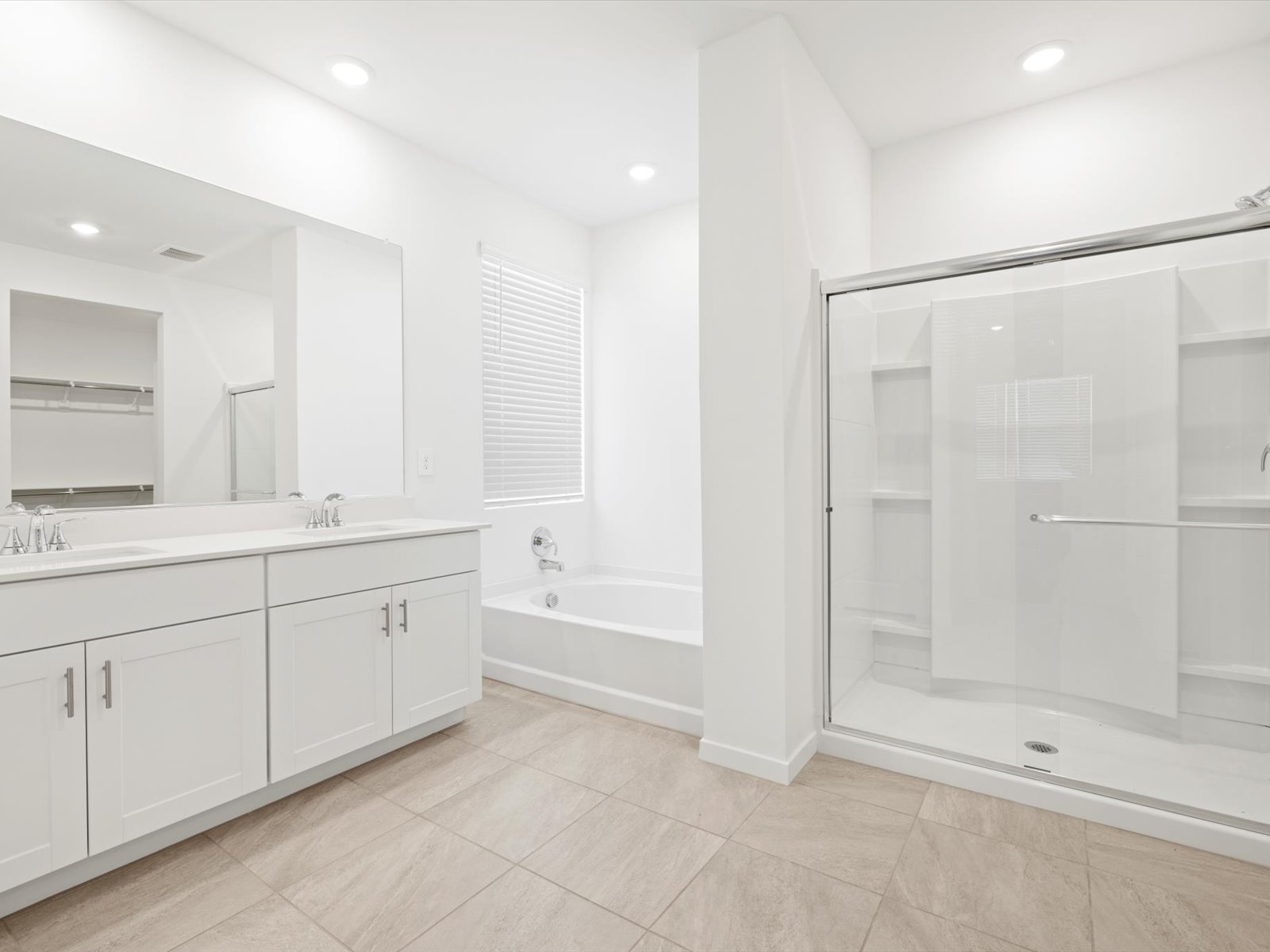 Bright bathroom with white cabinets, double sink, large mirror, bathtub, glass-enclosed shower, and beige tile floor.