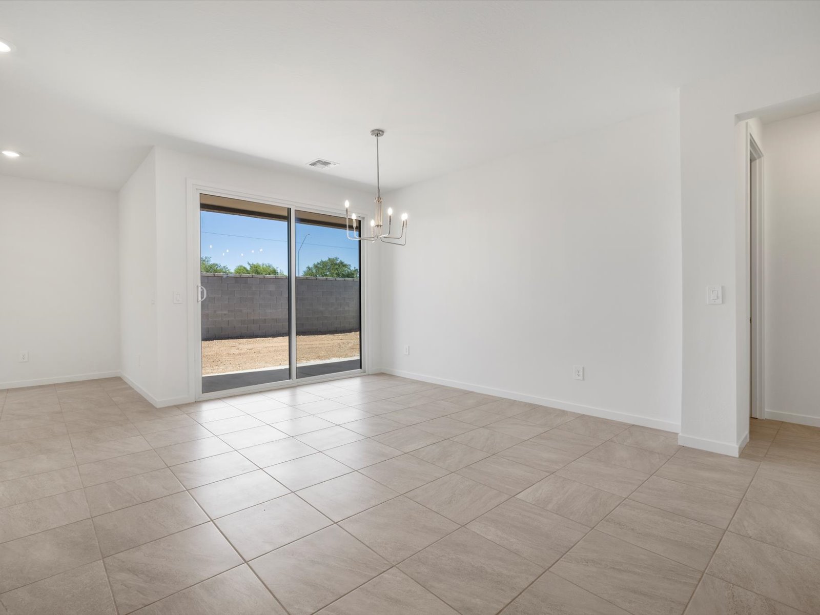Unfurnished room with tiled floors, white walls, a modern light fixture, sliding glass doors to a backyard, and an open doorway.