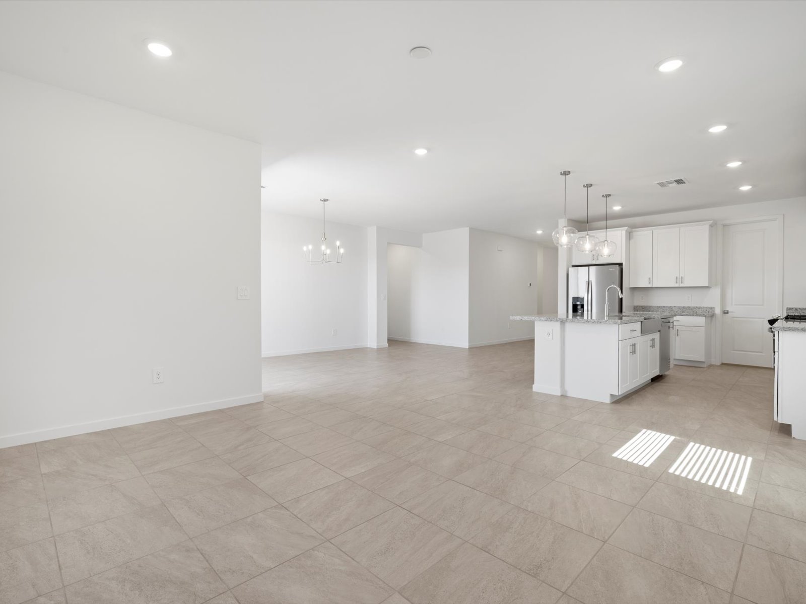 Spacious, unfurnished open-plan kitchen and living area with tiled floors, white walls, recessed lighting, and modern fixtures.