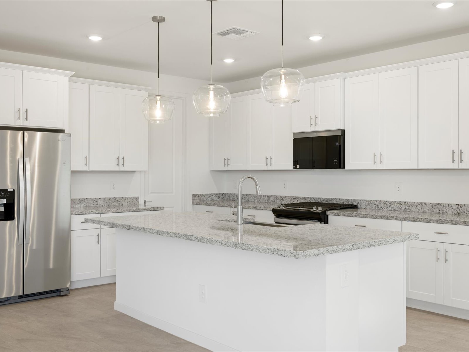 Modern kitchen with white cabinets, stainless steel appliances, granite countertops, a center island with sink, and three pendant lights hanging above the island.