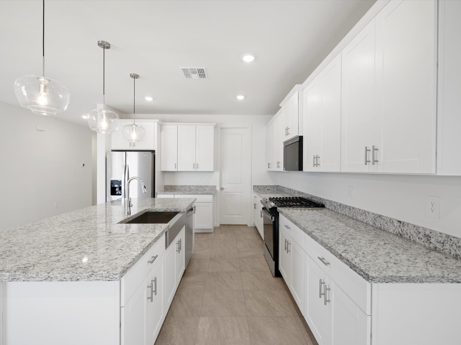 Modern kitchen with white cabinets, granite countertops, stainless steel appliances, island with sink, gas stove, and pendant lighting. Neutral tile flooring and recessed ceiling lights.