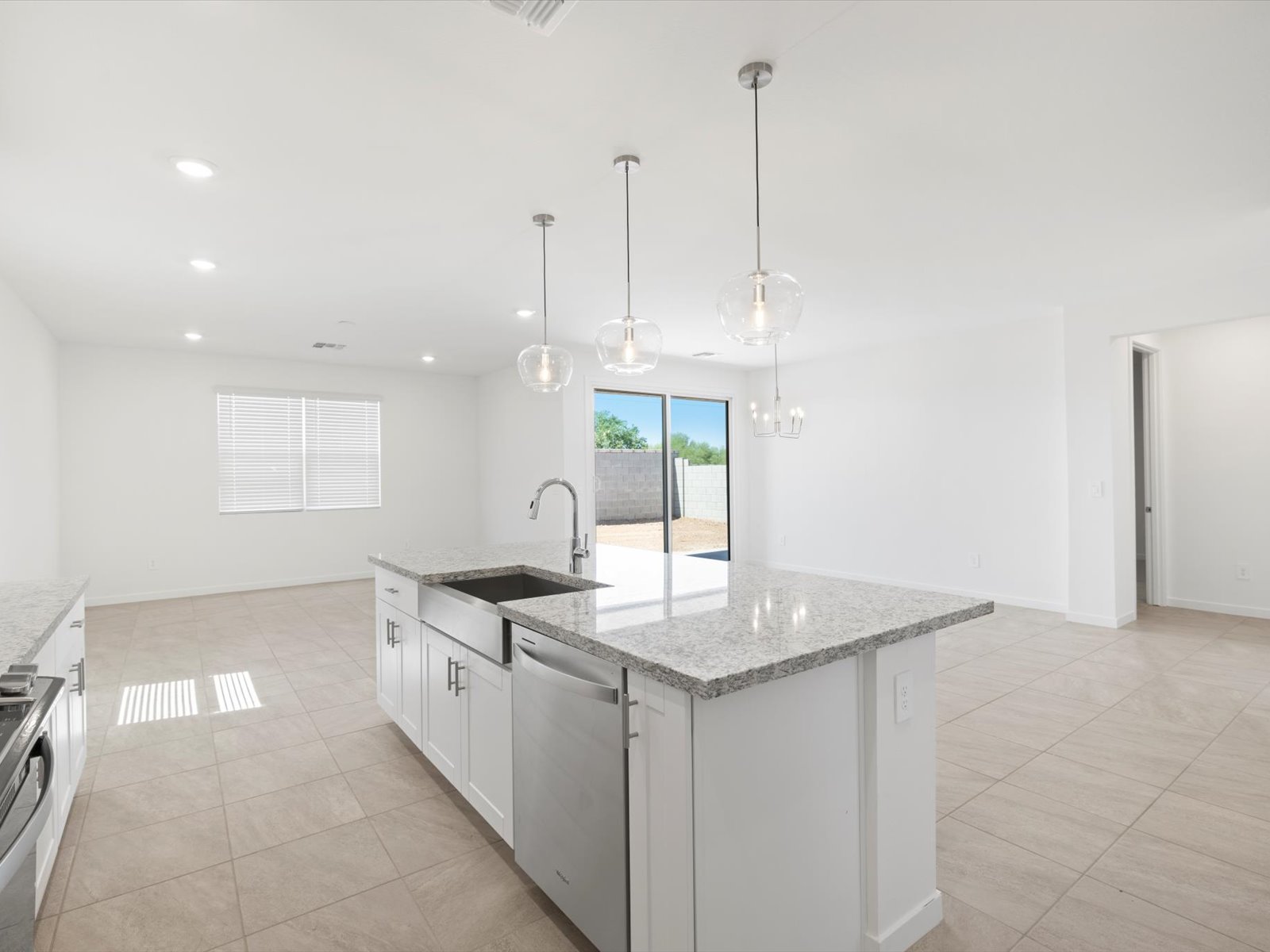 Modern kitchen with a large island, granite countertops, white cabinets, stainless steel appliances, pendant lights, and open layout leading to a backyard with sliding glass doors.