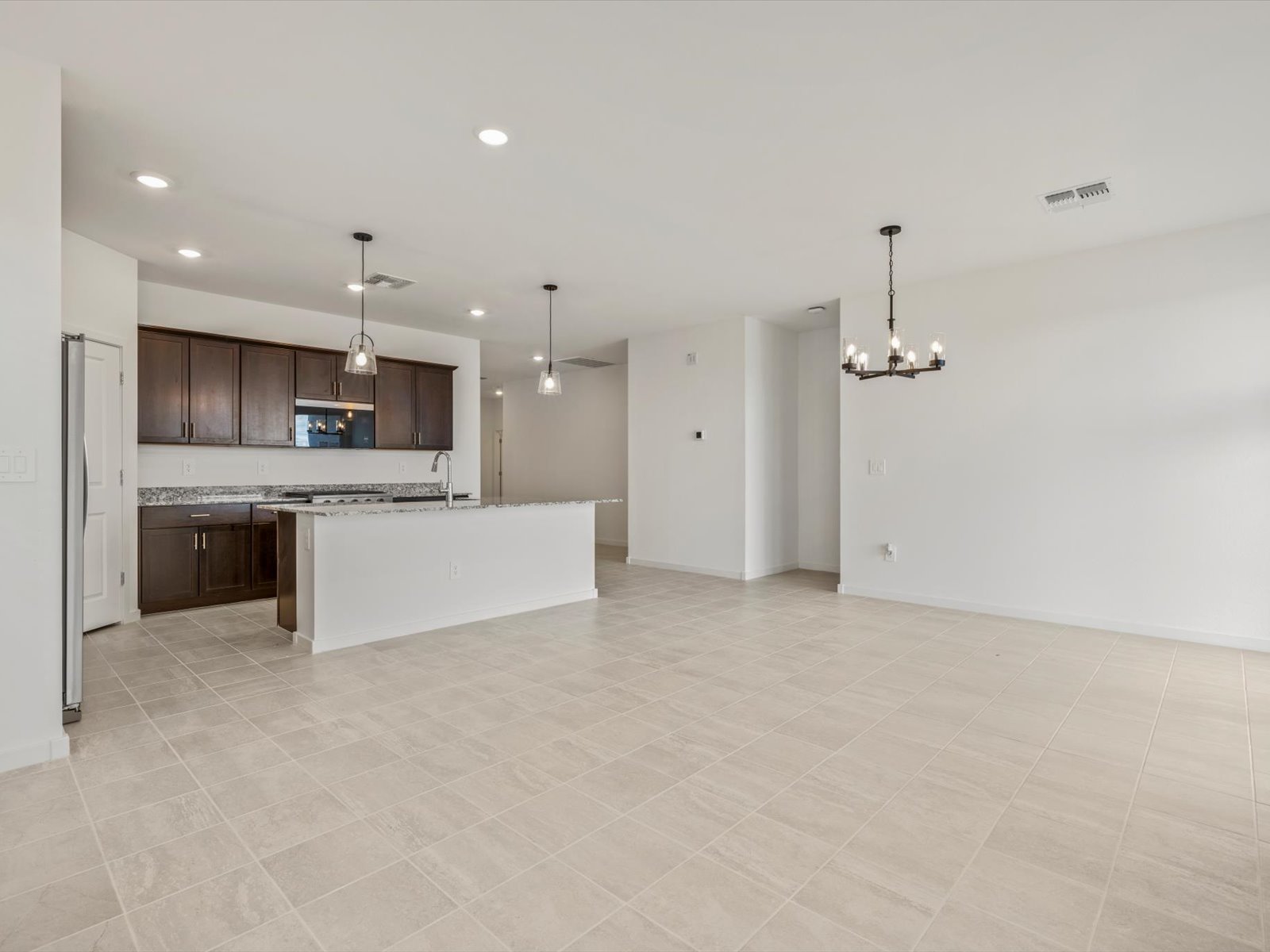Open-concept kitchen and living area with tile flooring, white walls, dark wood cabinets, granite countertops, and pendant lighting.