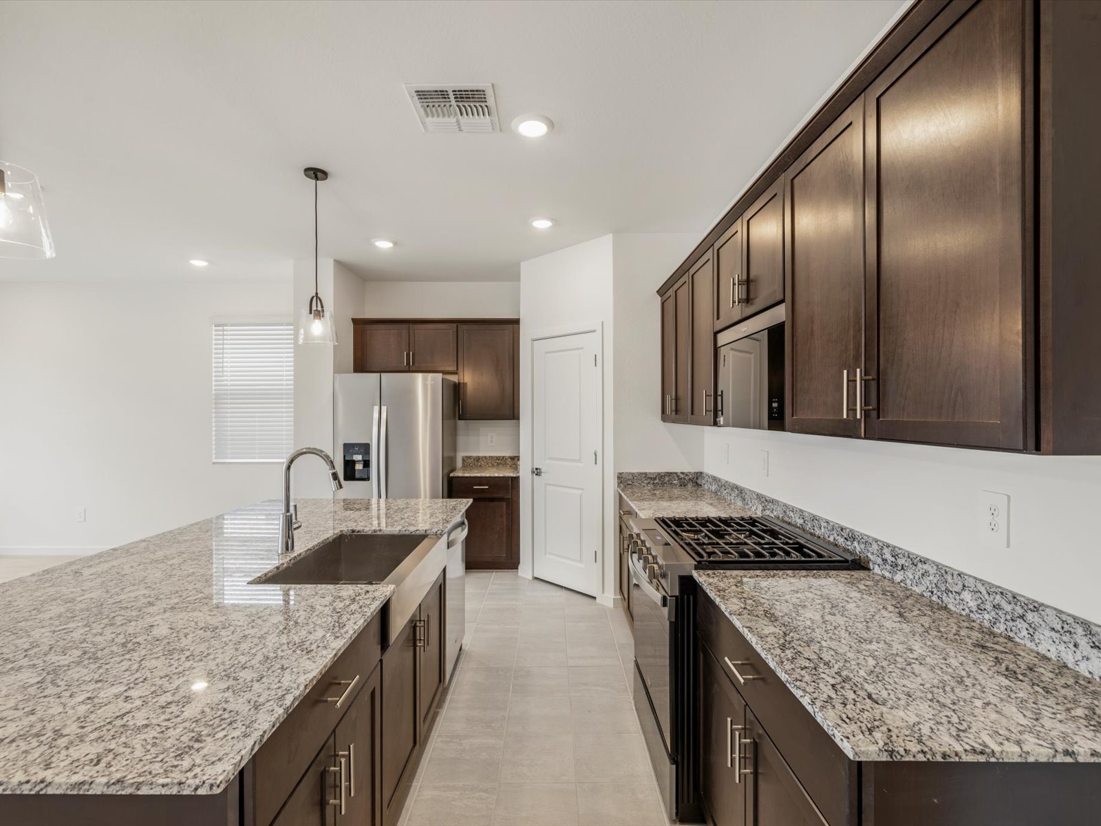 Modern kitchen with dark wood cabinets, stainless steel appliances, granite countertops, tile flooring, and a large island with a sink.