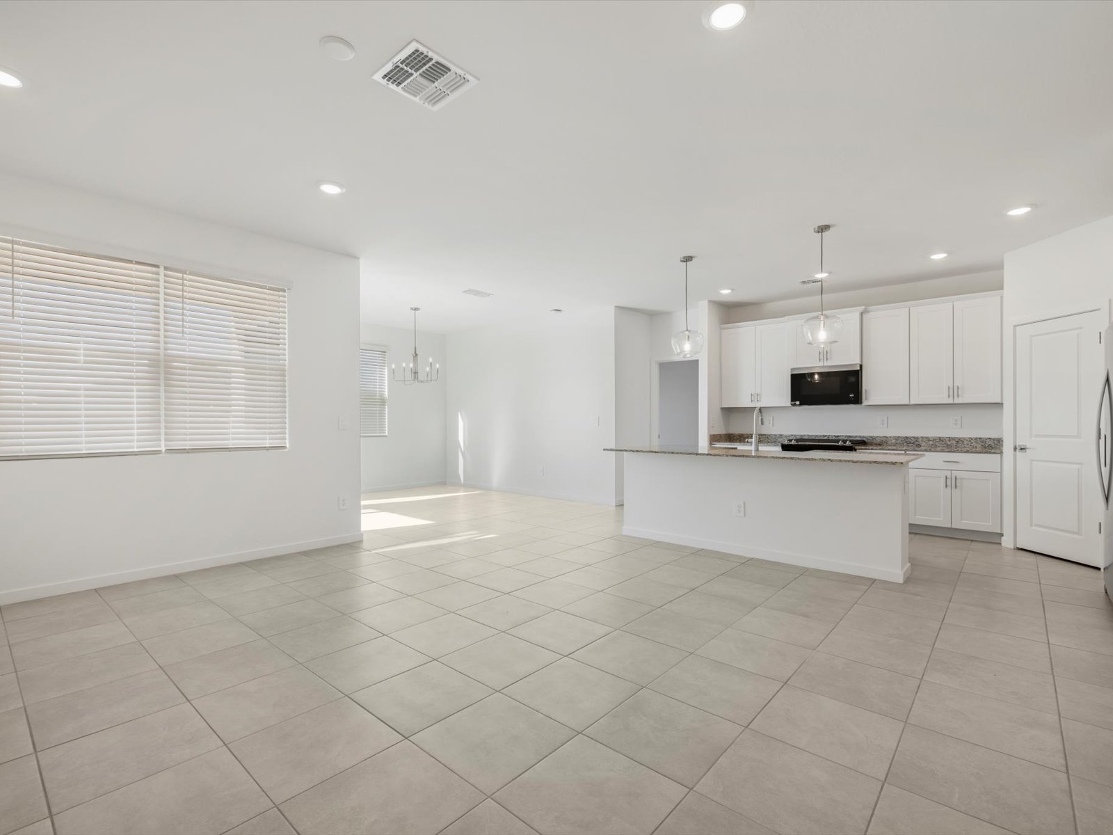 Modern, unfurnished open-plan kitchen and living area with tile flooring, white walls, large windows, recessed lighting, and stainless steel appliances.
