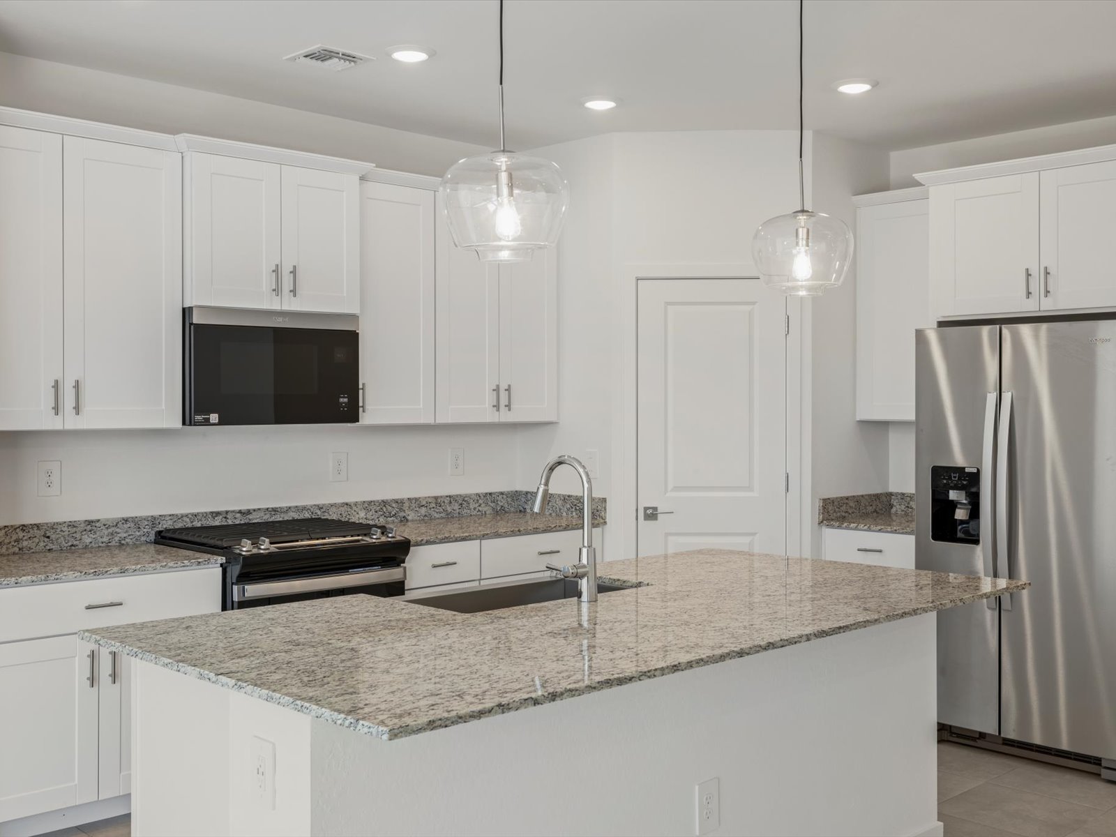 Modern kitchen with white cabinets, granite countertops, stainless steel appliances, a center island with a sink, and pendant lights overhead.