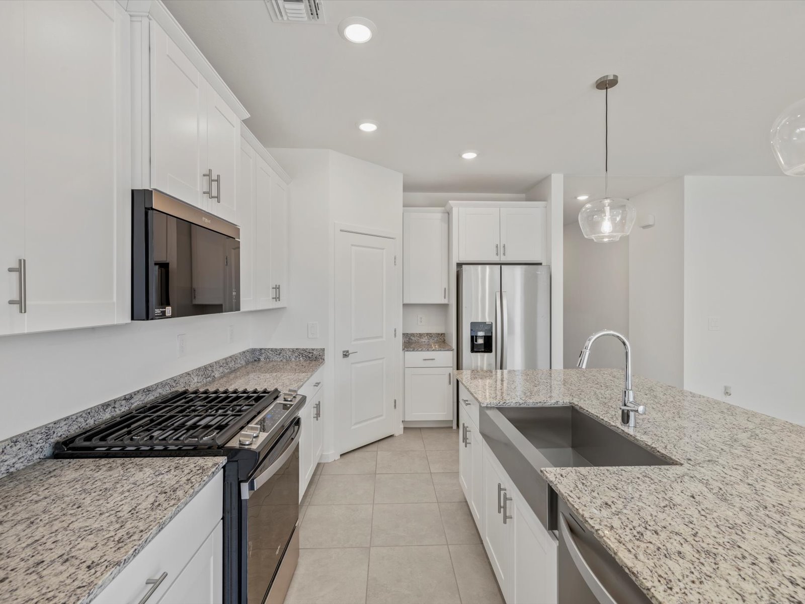 Modern kitchen with white cabinets, stainless steel appliances, granite countertops, a double sink, and pendant lighting over an island.
