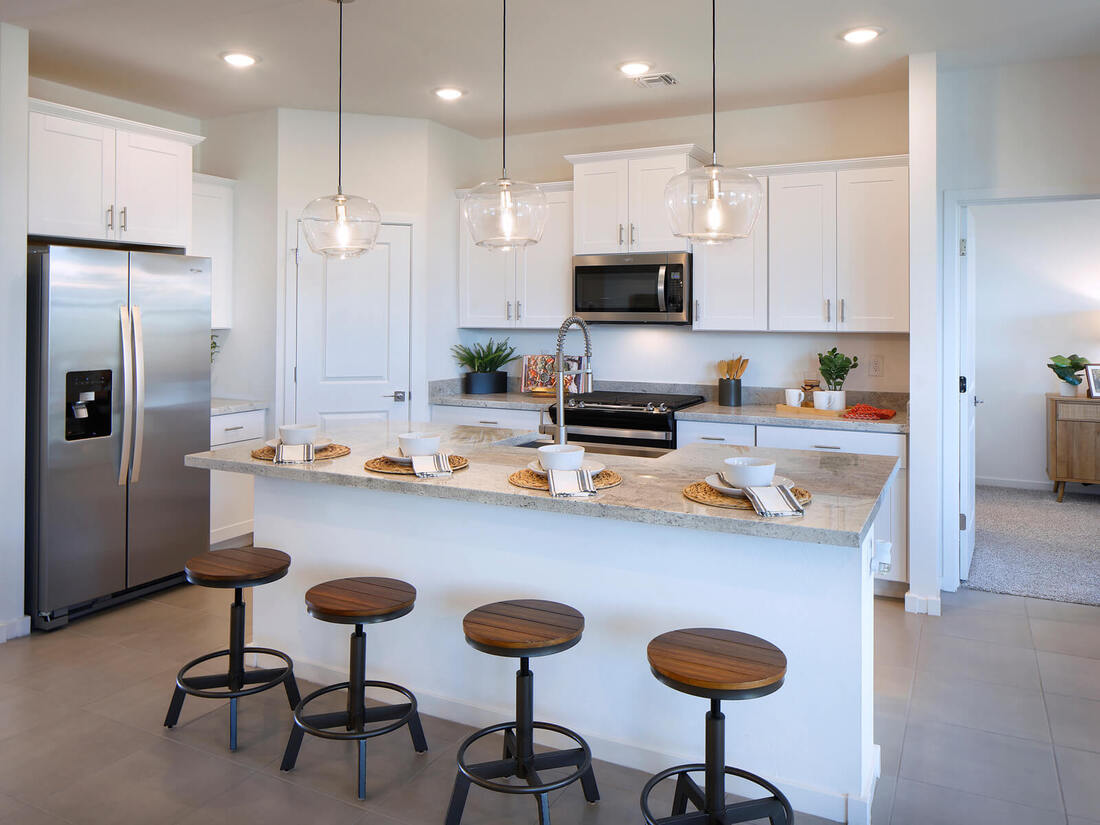 Modern kitchen with white cabinets, stainless steel appliances, an island with four wooden stools, pendant lights, and place settings for four.