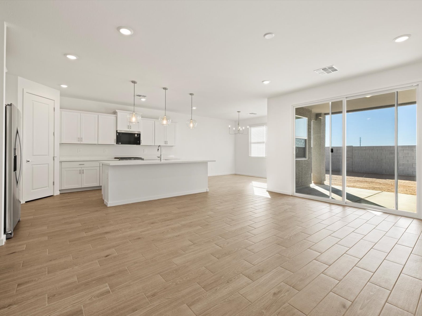 Spacious modern kitchen and living area with white cabinetry, stainless steel appliances, pendant lights, tile flooring, and large sliding glass doors opening to a backyard patio.