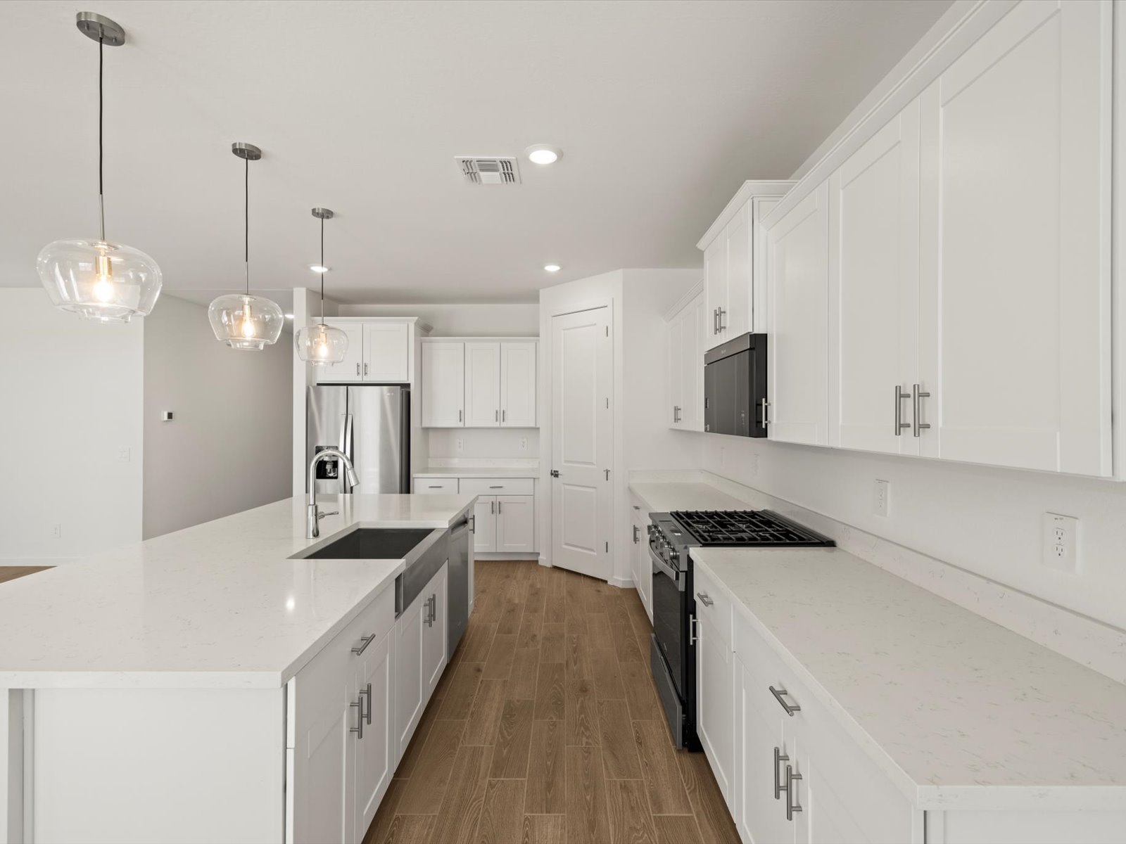Modern kitchen with white cabinets, stainless steel appliances, a large island with a sink, pendant lights, and wood flooring.