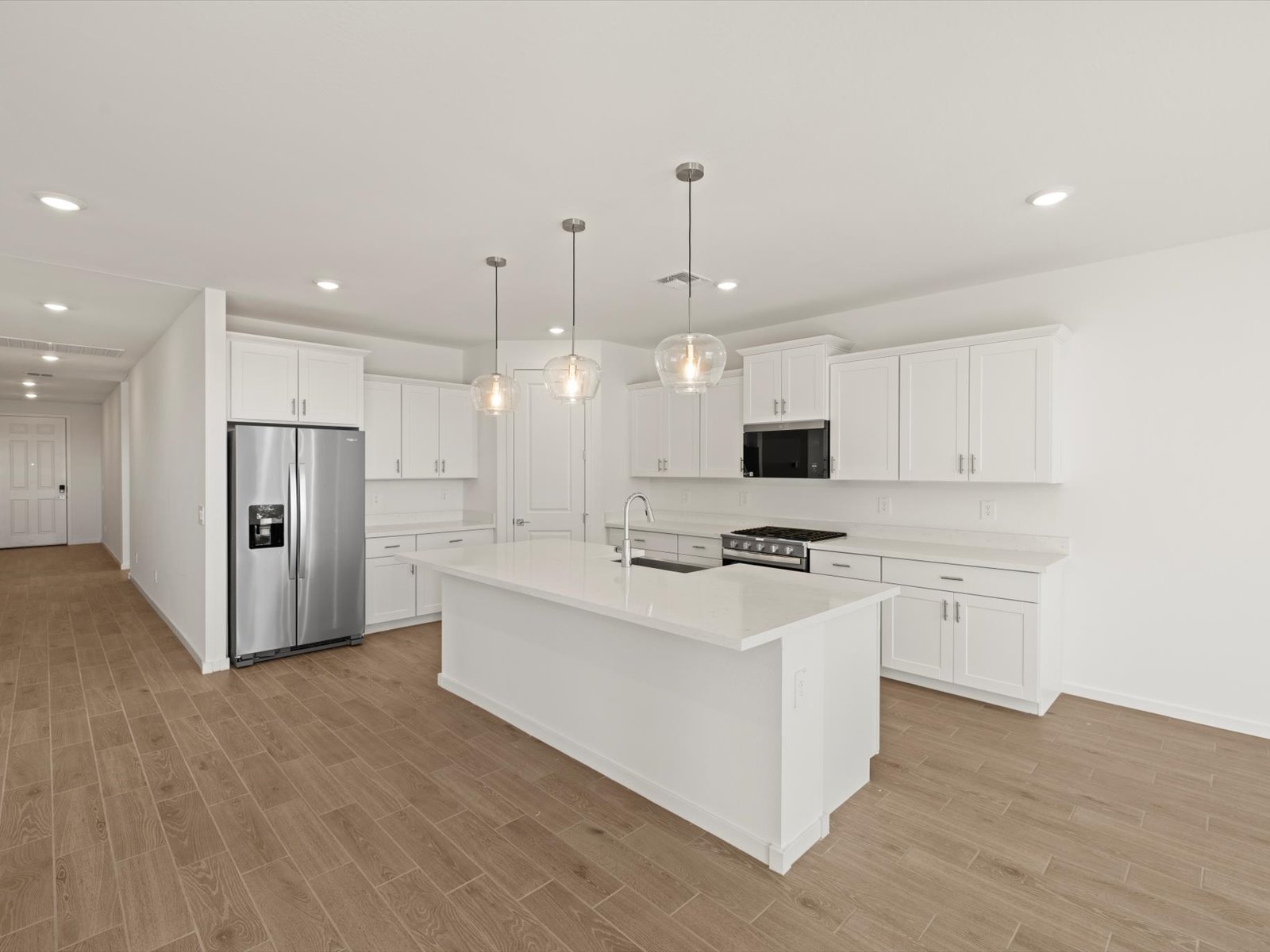 Modern kitchen with white cabinets, stainless steel appliances, an island with pendant lights, and wood-look tile flooring.