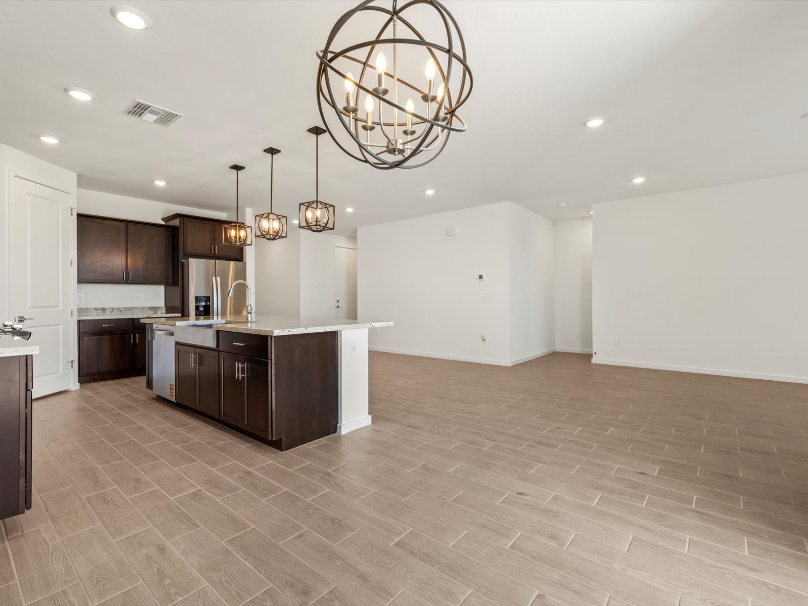 Modern open kitchen and living area with brown cabinets, island, pendant lights, tile flooring, and white walls.