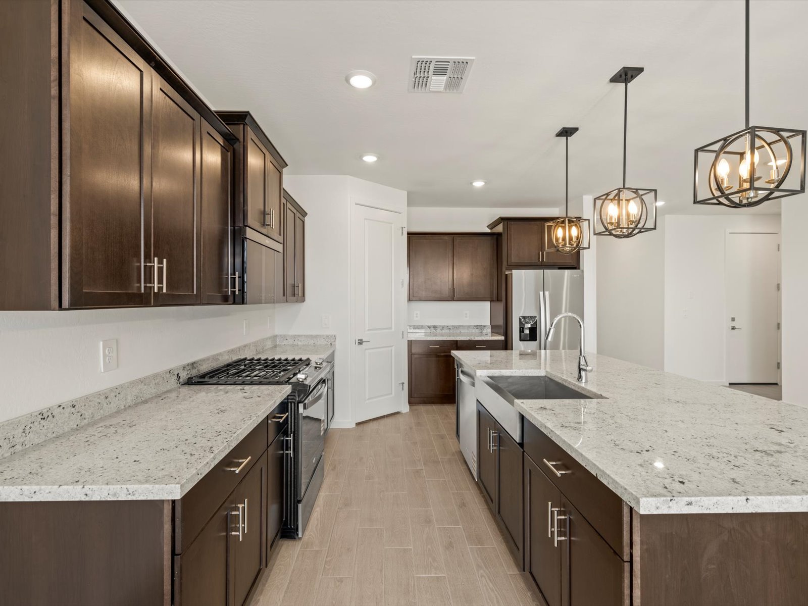 Modern kitchen with dark wood cabinets, light granite countertops, stainless steel appliances, and pendant lights over a large island.