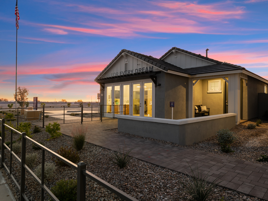 A modern single-story building with large windows and a porch, set against a sunset sky, surrounded by landscaping and a paved walkway.