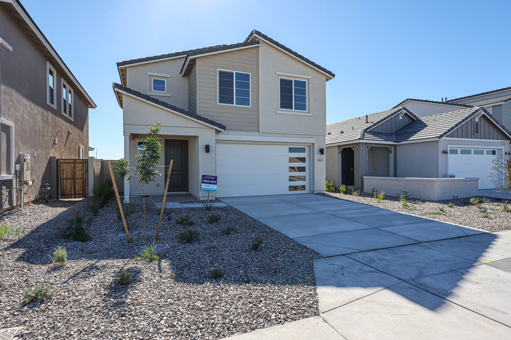 Two-story modern house with cream and beige exterior, double garage, covered entry, and gravel landscaping in the front yard on a sunny day.