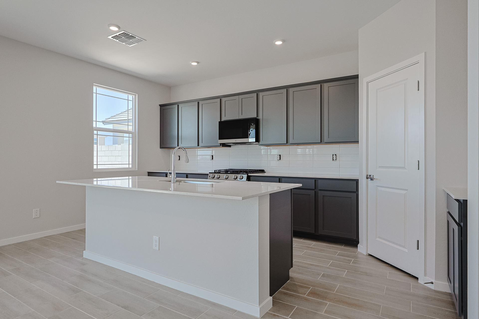 Modern kitchen with dark cabinets, white countertops, an island, stainless steel appliances, tile flooring, and a window providing natural light.