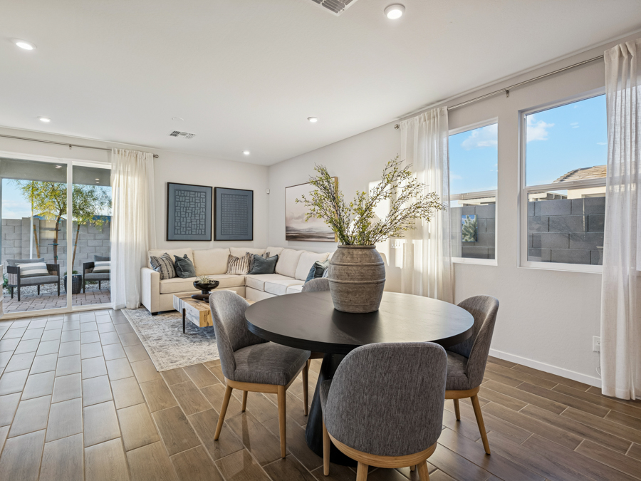 Open-plan living and dining area with a round table, gray chairs, beige sectional sofa, large windows, and sliding glass door to a patio.