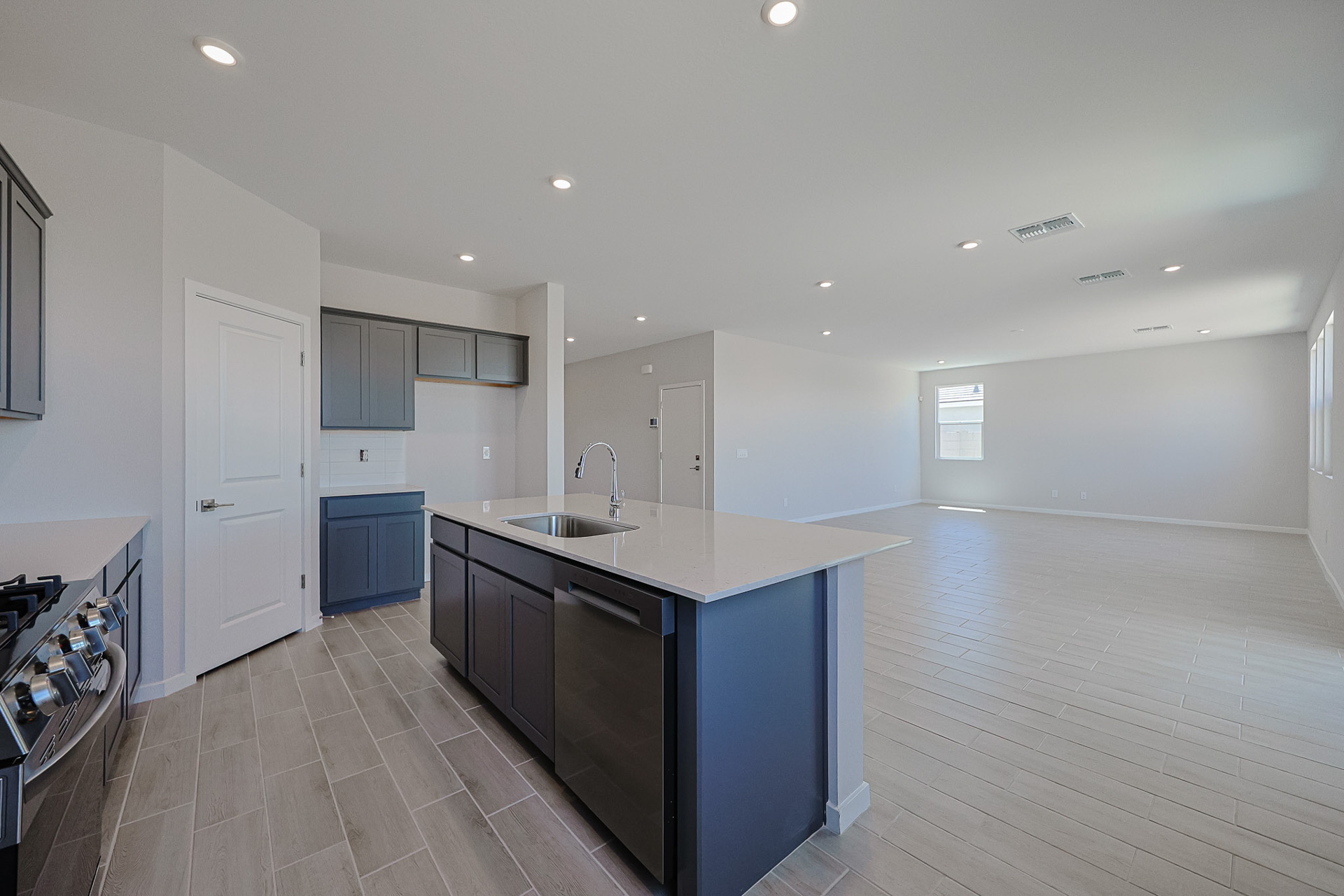 Modern open-concept kitchen and living area with tile flooring, gray cabinets, stainless steel appliances, and large windows letting in natural light.