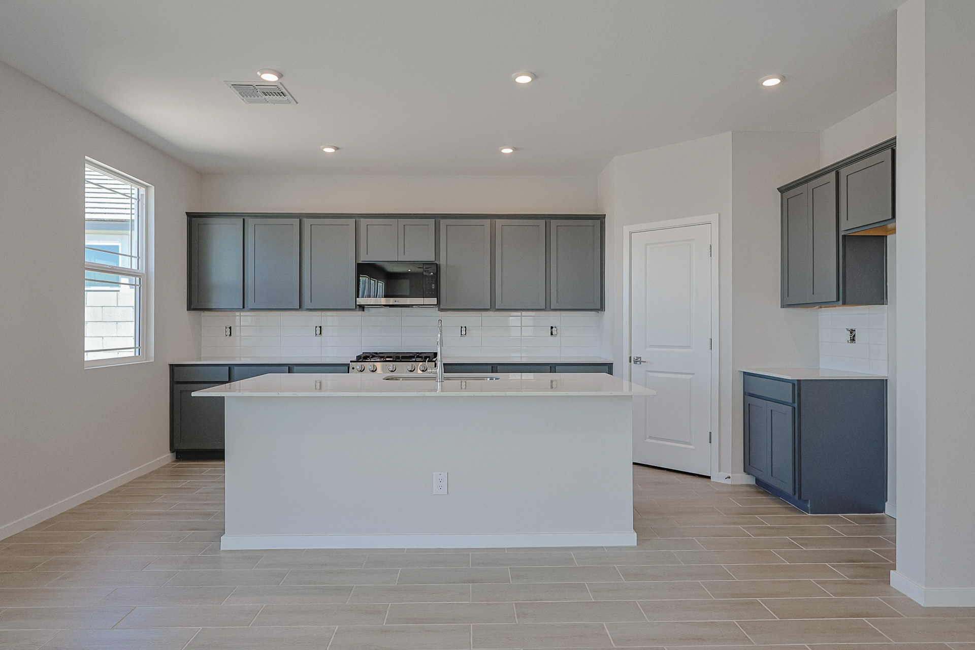 Modern kitchen with gray cabinets, white countertops, a center island, gas stove, built-in microwave, and tile flooring. White subway tile backsplash and neutral wall colors.