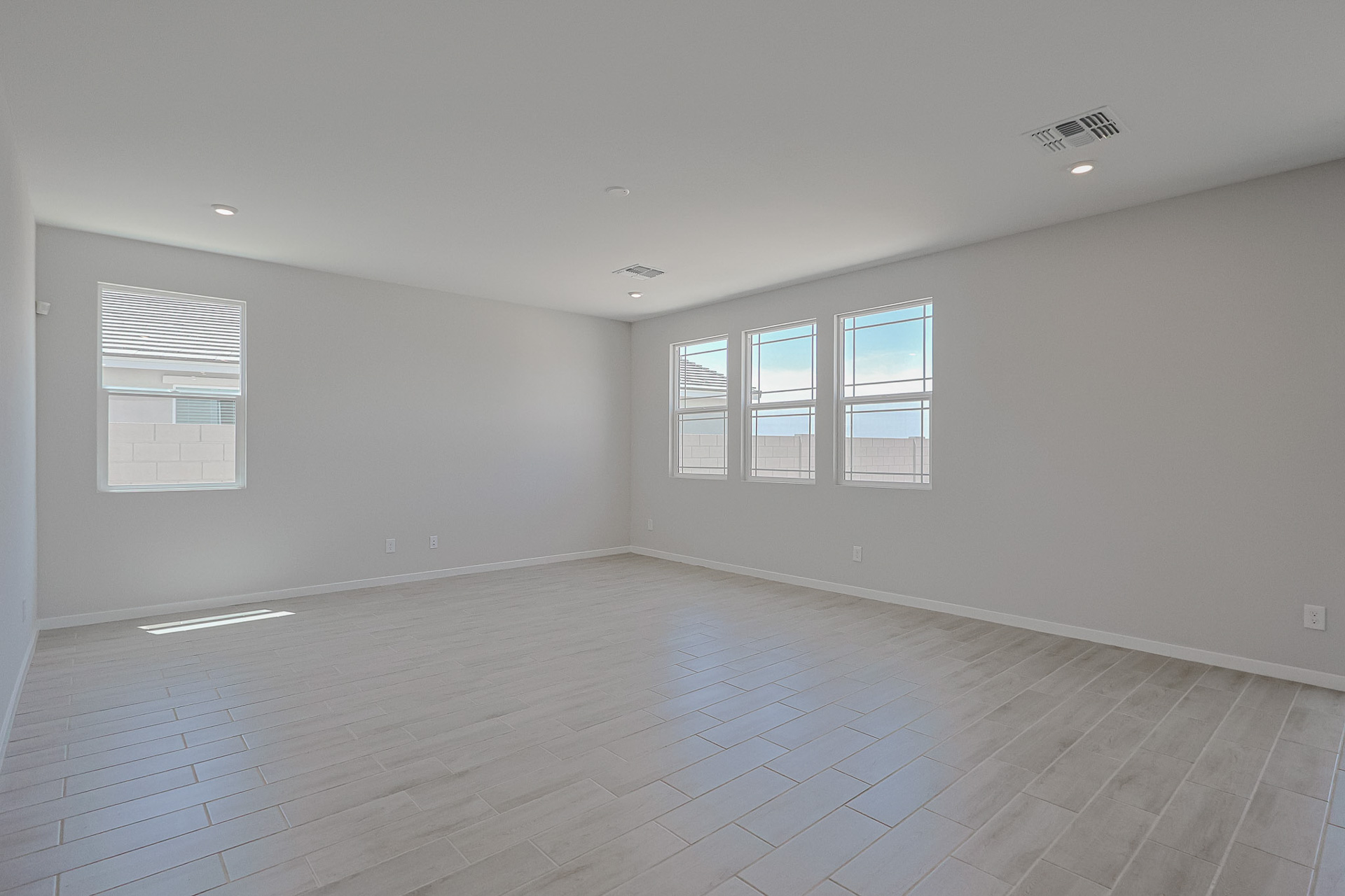 Empty room with light-colored tile flooring, white walls, recessed lighting, and multiple windows letting in natural light.