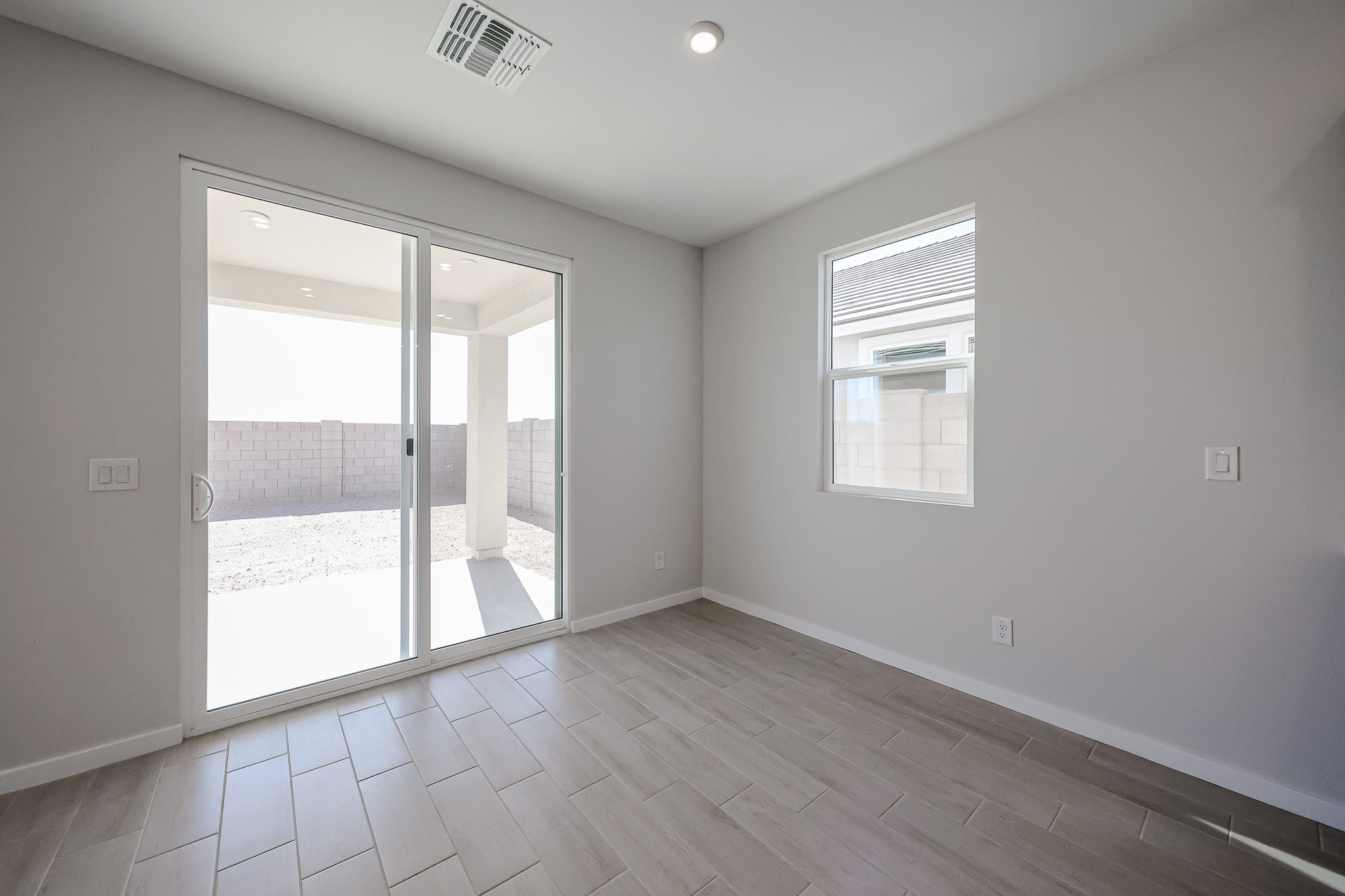 Empty room with light gray walls, a tiled floor, a small window, and large sliding glass doors leading to a fenced backyard with gravel.