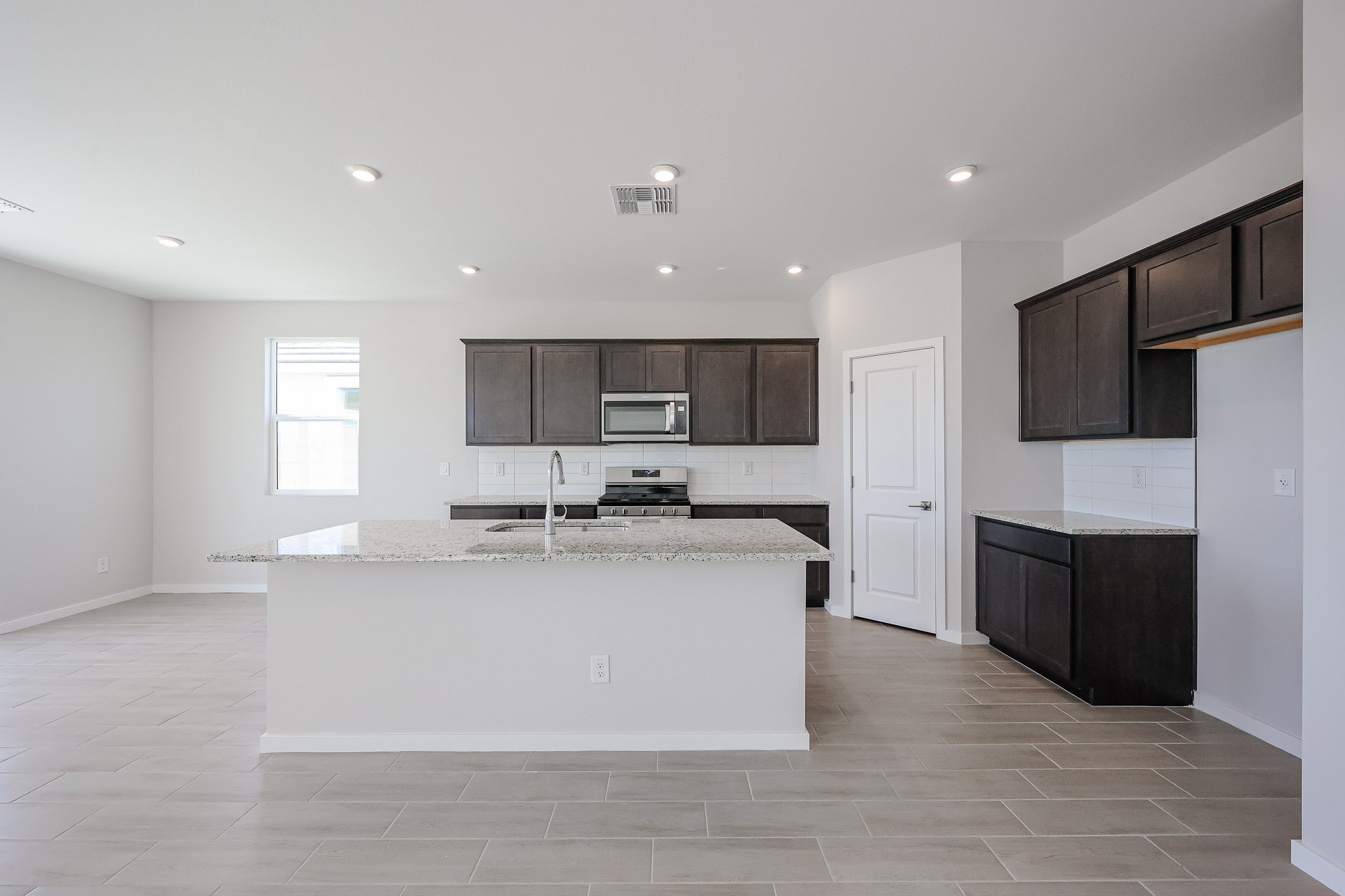 Modern kitchen with dark wood cabinets, stainless steel appliances, granite countertops, and light tile flooring under recessed lighting.