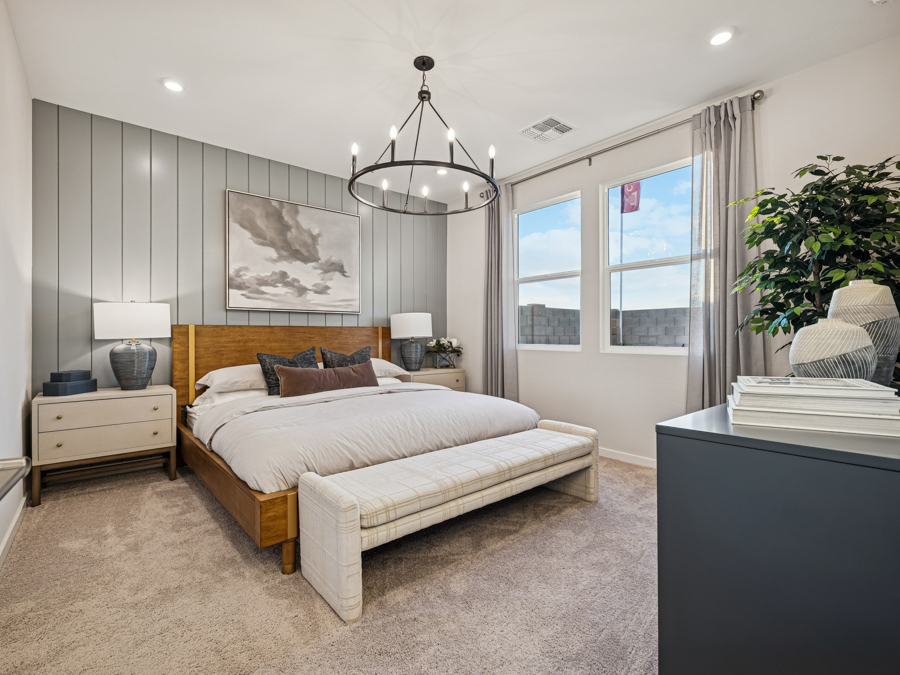 Modern bedroom with a wooden bed, gray paneled accent wall, large window, chandelier, bench at the foot of the bed, and neutral decor.