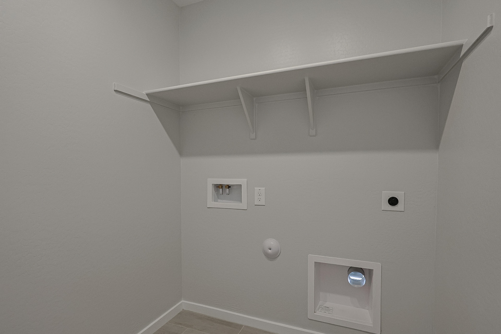 Empty laundry room with gray walls, a shelf, and hookups for a washer and dryer. No appliances are present.