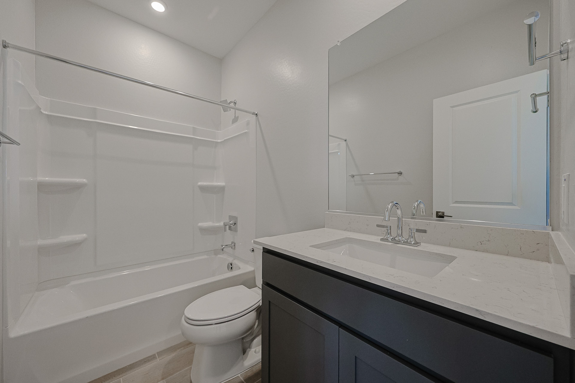 Modern bathroom with a bathtub-shower combo, white toilet, light countertop with sink, large mirror, and gray vanity cabinets.