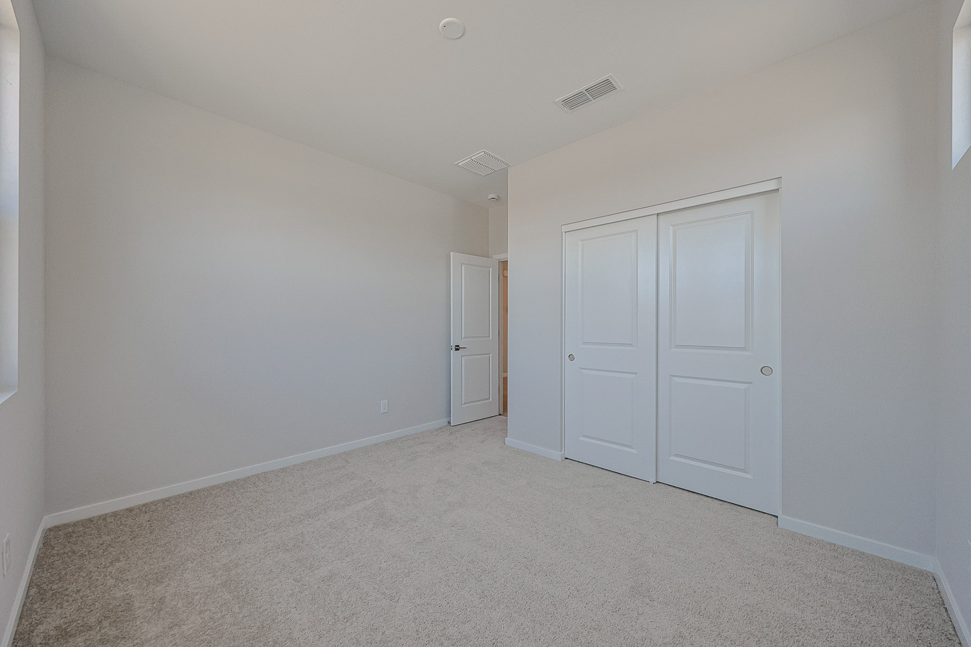 Empty room with light beige carpet, white walls, a closet with sliding doors, and an open door leading to a hallway.