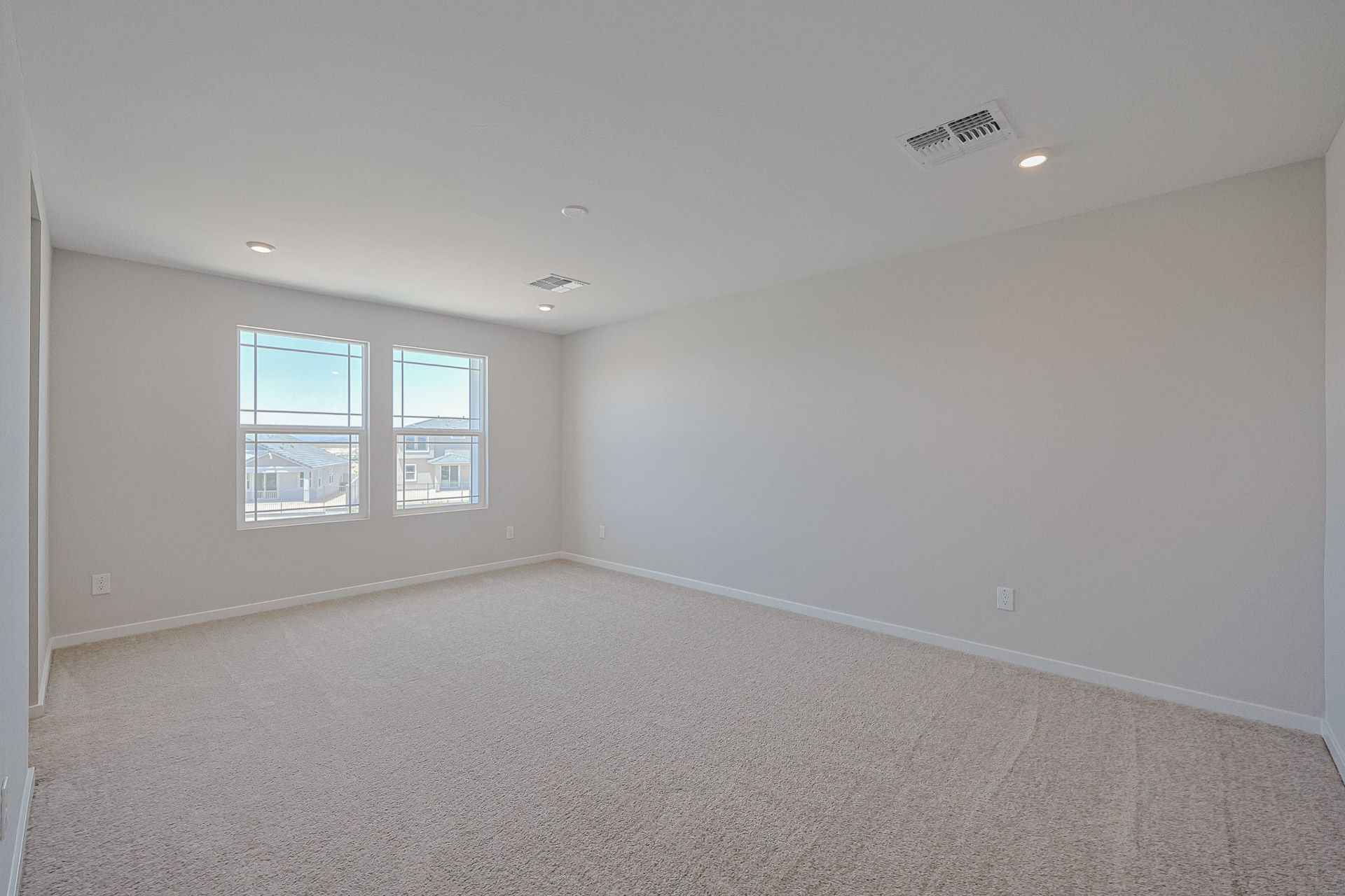 Empty room with beige carpet, white walls, two windows letting in natural light, and ceiling vents with recessed lighting visible.