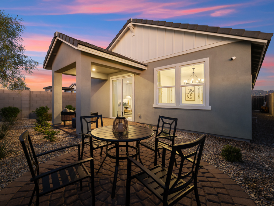Single-story house at sunset with a covered patio, large window, and outdoor seating area on a circular brick patio, surrounded by gravel landscaping.