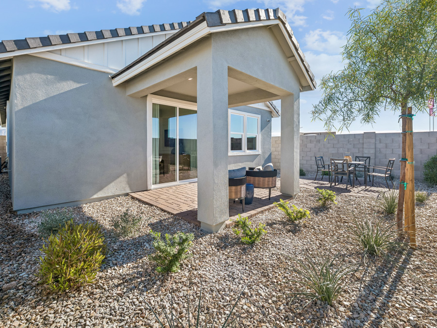 Single-story house with covered patio, sliding glass door, outdoor seating, gravel landscaping, and a small dining area on a sunny day.