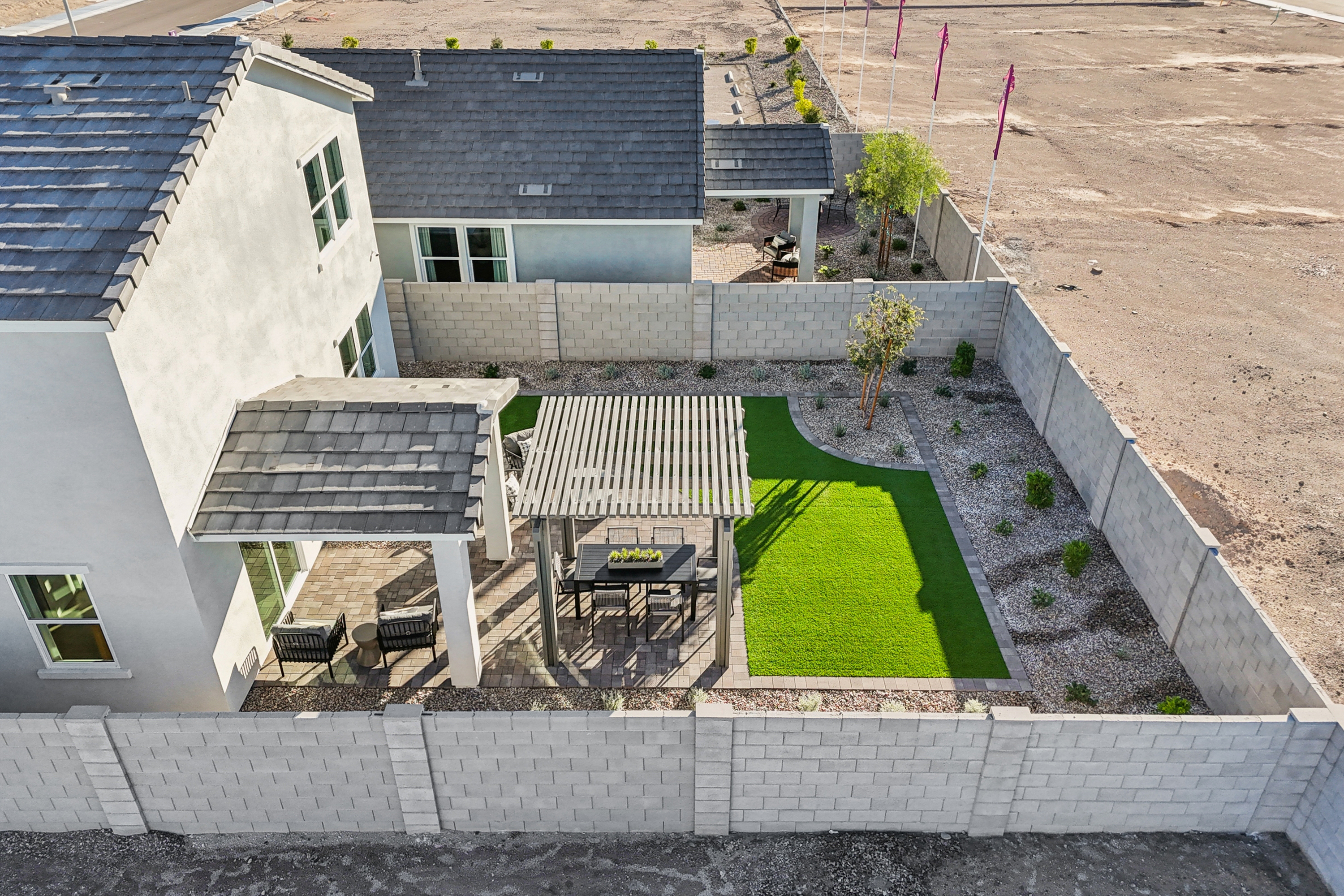 Aerial view of a modern backyard with artificial grass, a pergola over an outdoor dining area, gravel landscaping, and concrete block walls surrounding the yard.