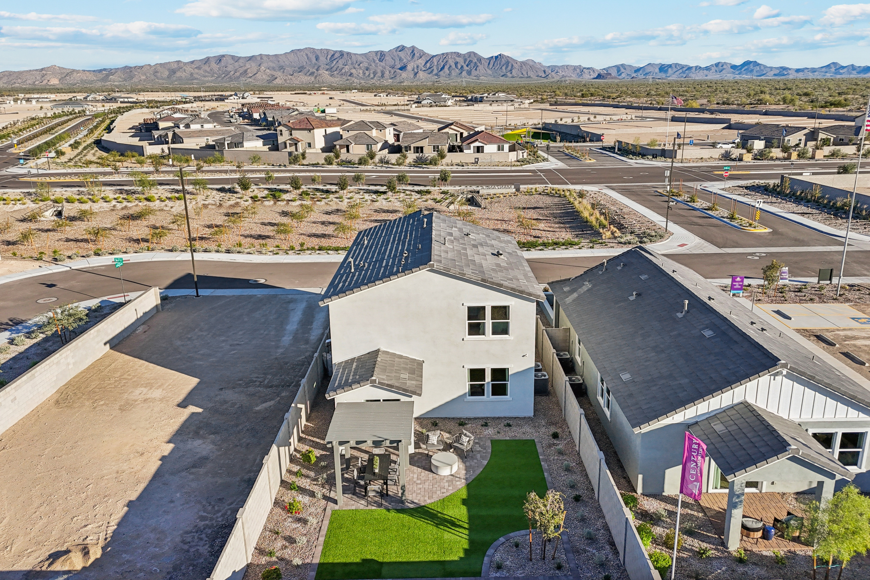 Aerial view of a two-story house with solar panels, artificial grass backyard, and desert landscaping in a suburban neighborhood with mountains in the background.