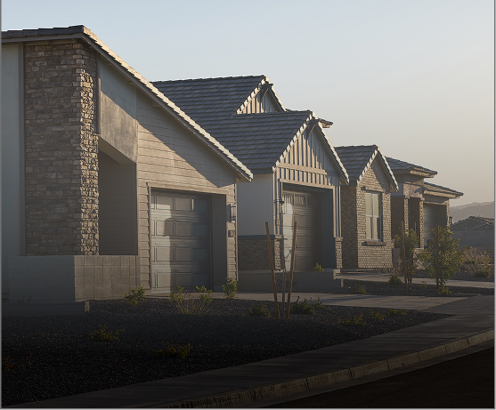 Row of modern, single-story suburban houses with garages and landscaped front yards, photographed in early morning light.